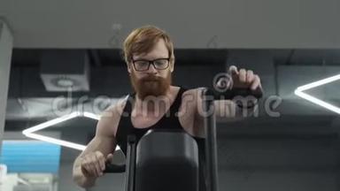 红发男子骑自行车训练有氧运动。 在健身房里用旋转自行车的人